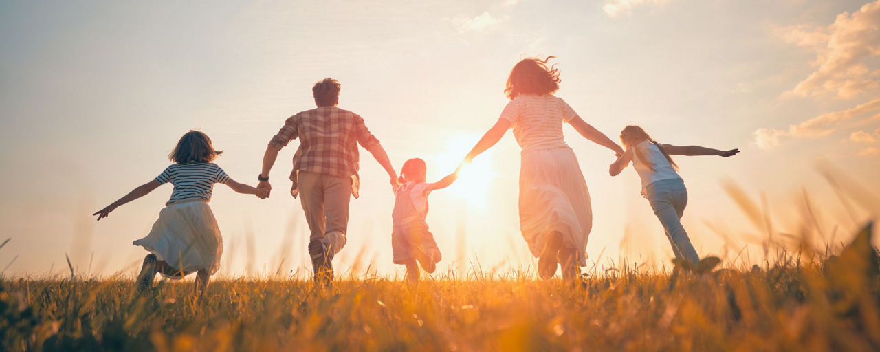 Eine Familie springt Hand in Hand über eine Wiese
