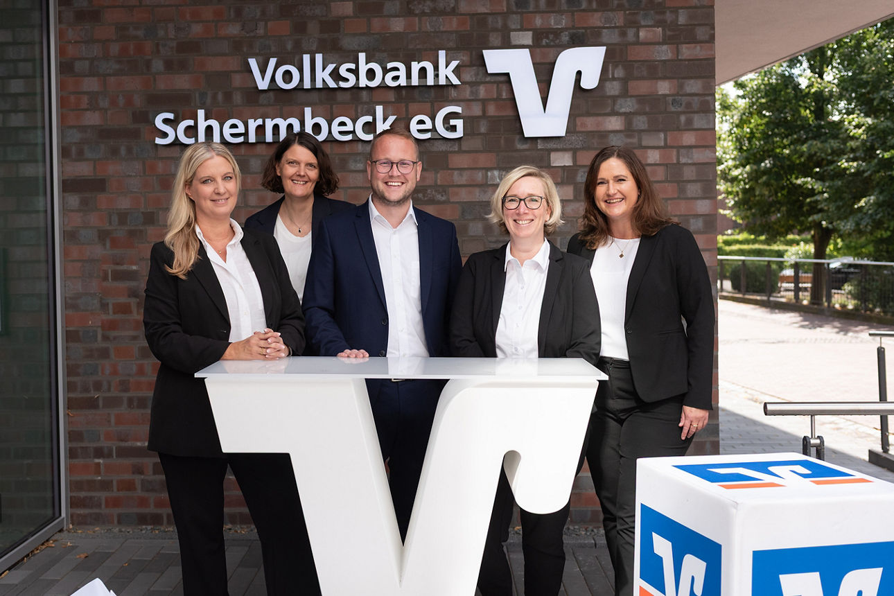 Gruppenfoto unserer Serviceberater mit Sebastian Kemmesies als Leiter in der Mitte unserer 4 Beraterinnen. vor dem Schriftzug Volksbank Schermbeck eG.