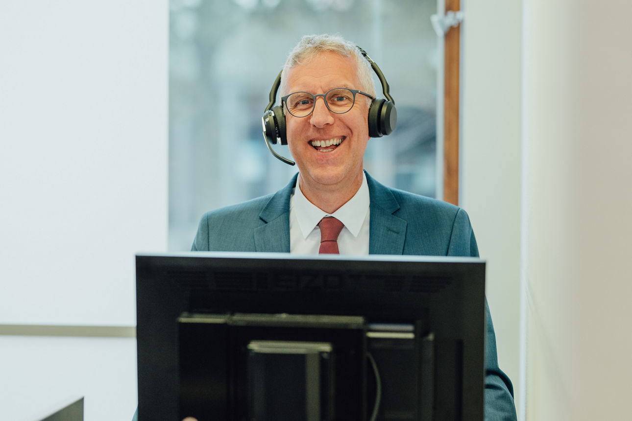 Ein Mitarbeiter lacht mit dem Headset in die Kamera
