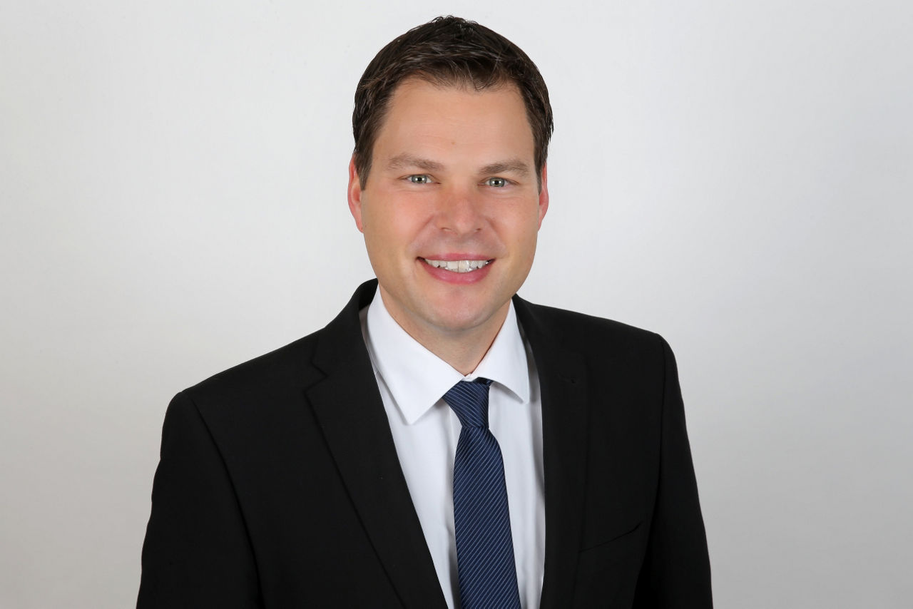 Ein lächelnder Mann in einem Anzug schaut in die Kamera.