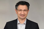 Sedat Sevis hat schwarze kurze Haare und eine Brille. Er trägt einen Anzug.