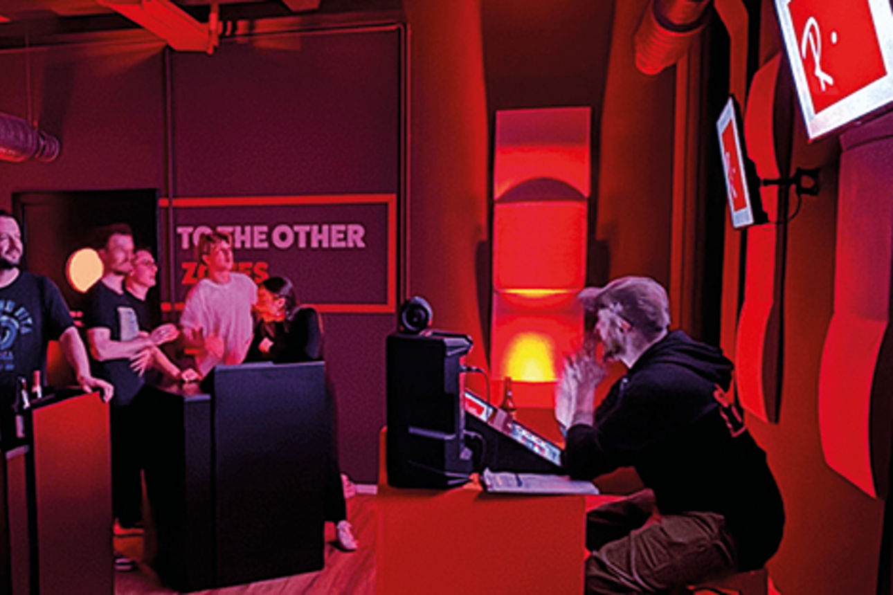 In einem Raum stehen zwei Pulte mit mehreren Personen dahinter, die eine Gamesho spielen.