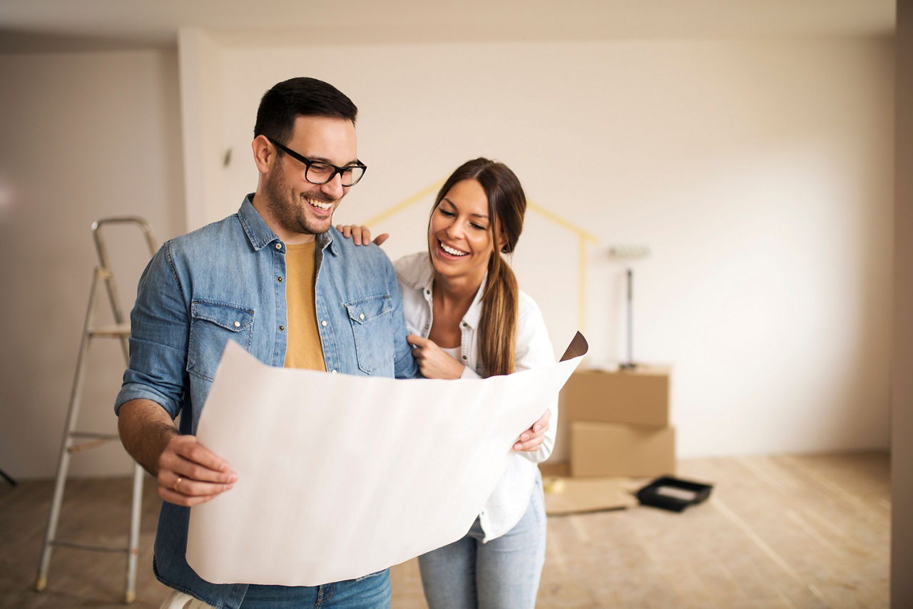 Ein Pärchen schaut lächelnd auf Baupläne