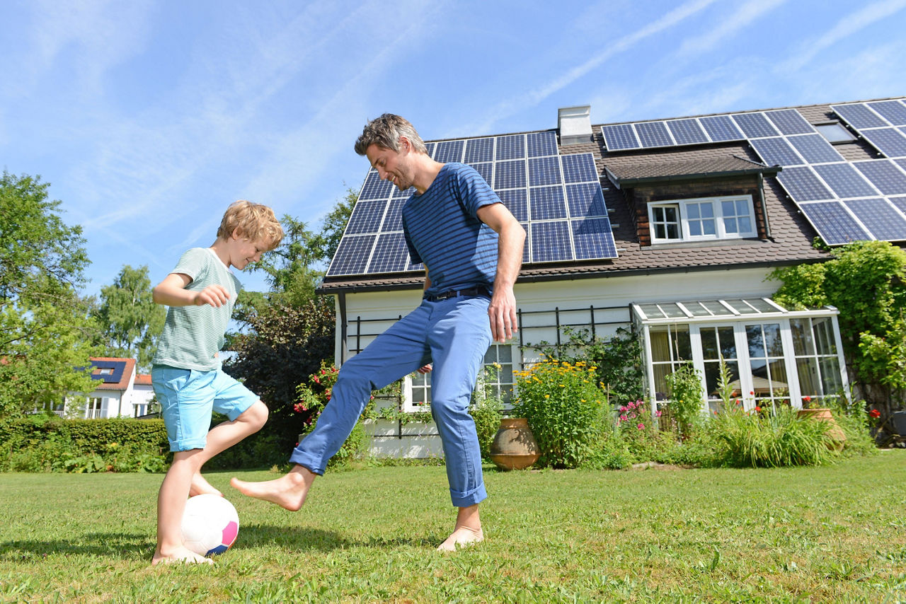 Vater und Sohn spielen Fußball im Garten vor dem Haus mit Solardach