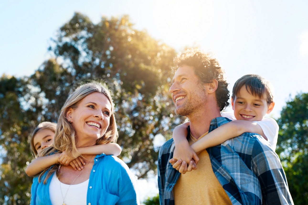Glückliche Familie mit zwei Kindern, die draußen in der Natur lacht und Spaß hat.
