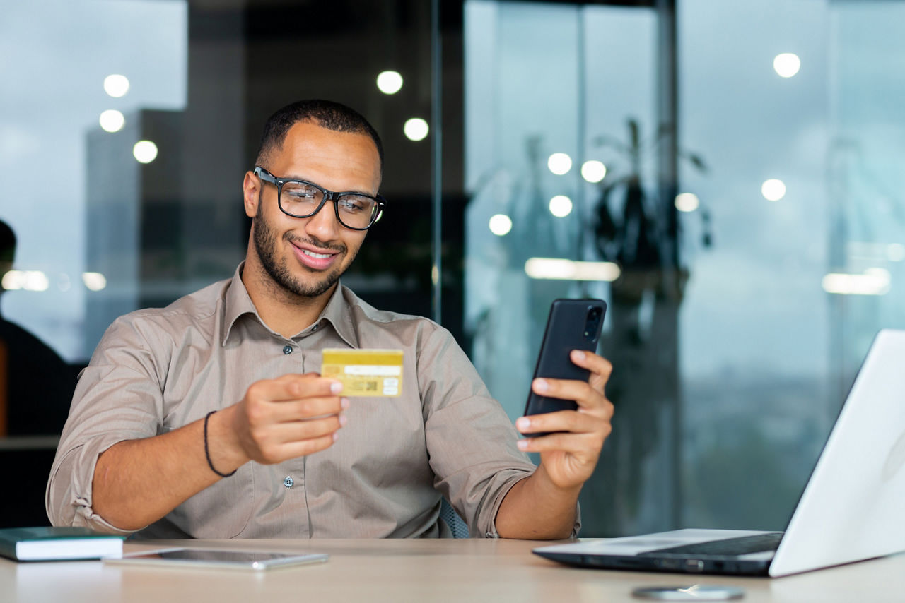 Mann vor einem Laptop mit einer Bankkarte und einem Smartphone