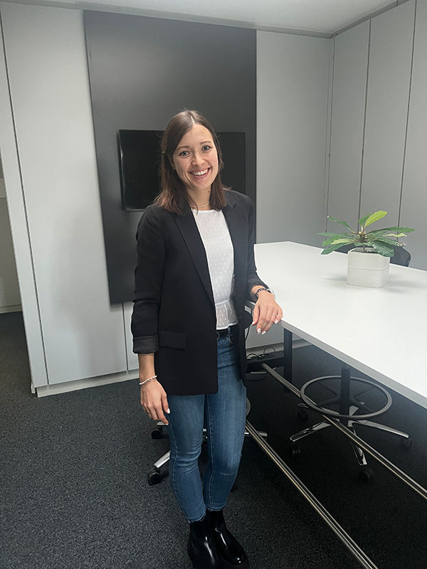 Junge Frau mit halblangen dunklen Haaren steht im Büro an einem Stehttisch gelehnt