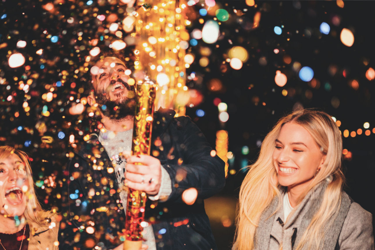Drei Personen feiern das neue Jahr in einer bunten Konfettiwolke.