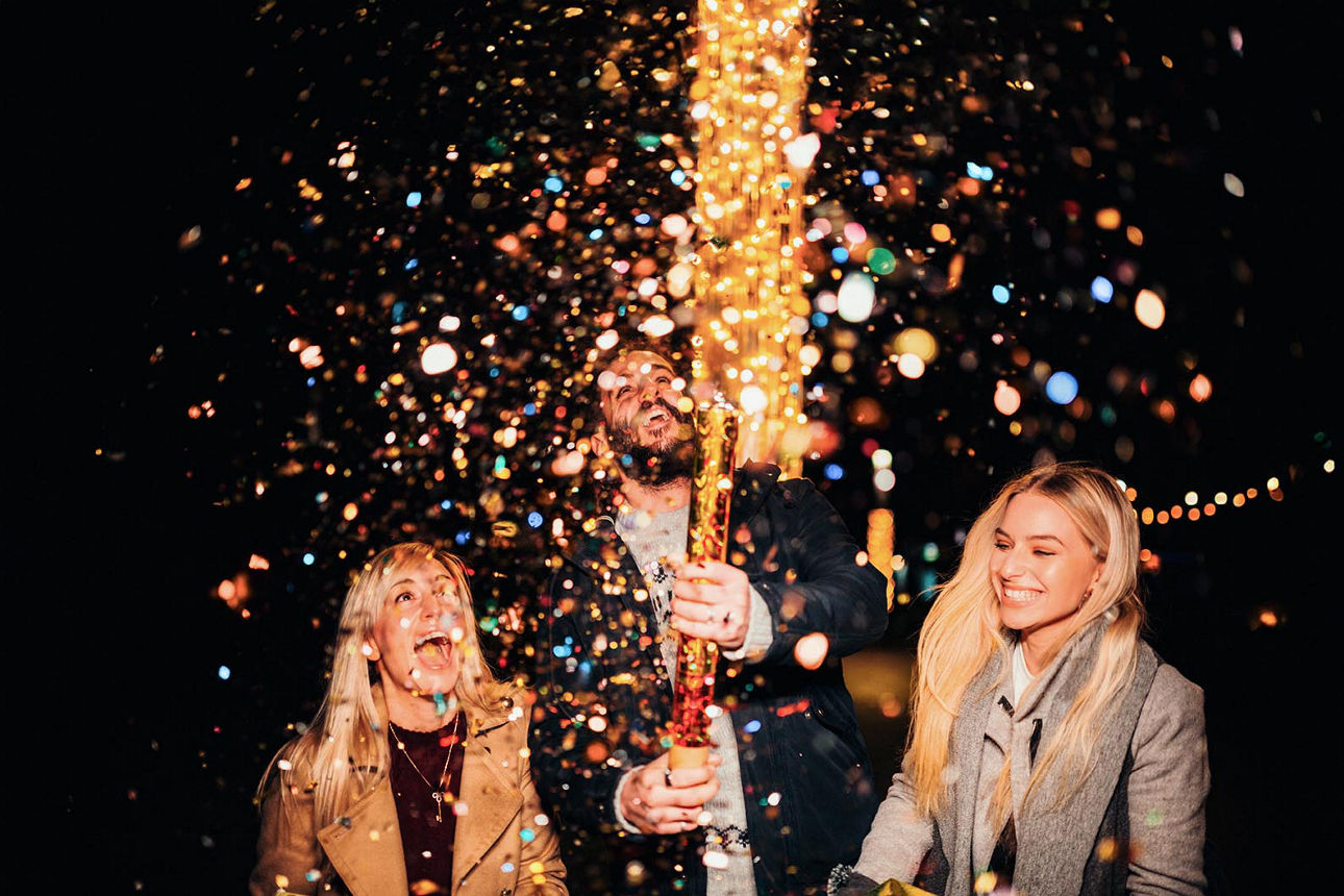 Frauen und Männer stehen lachend mit brennenden Wunderkerzen in den Händen beieinander.