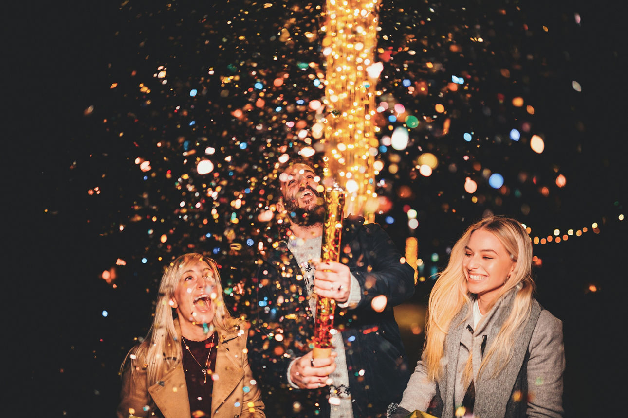 Drei Personen feiern den Jahreswechsel mit Feuerwerk