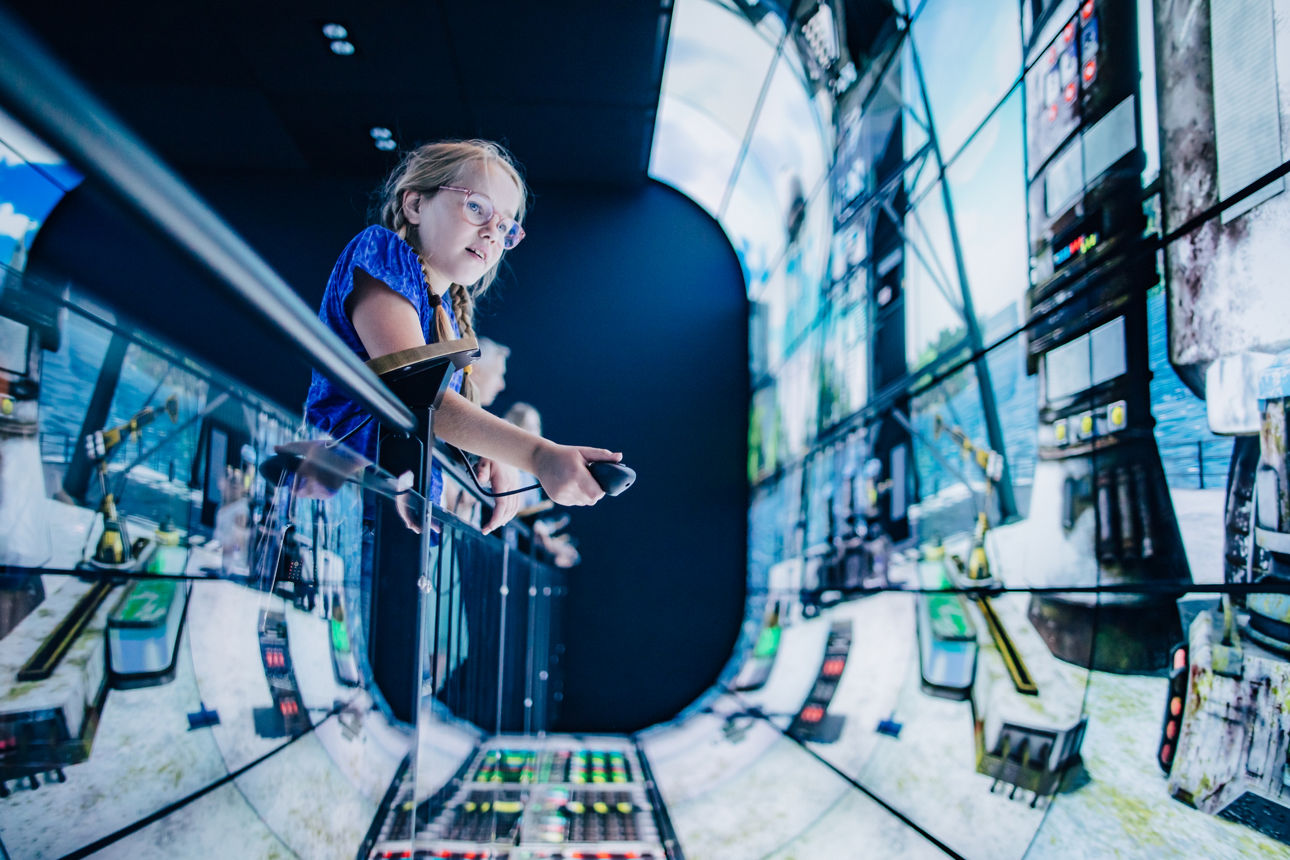 Kind steht in Spacekapsel und hat eine Fernbedienung in der Hand