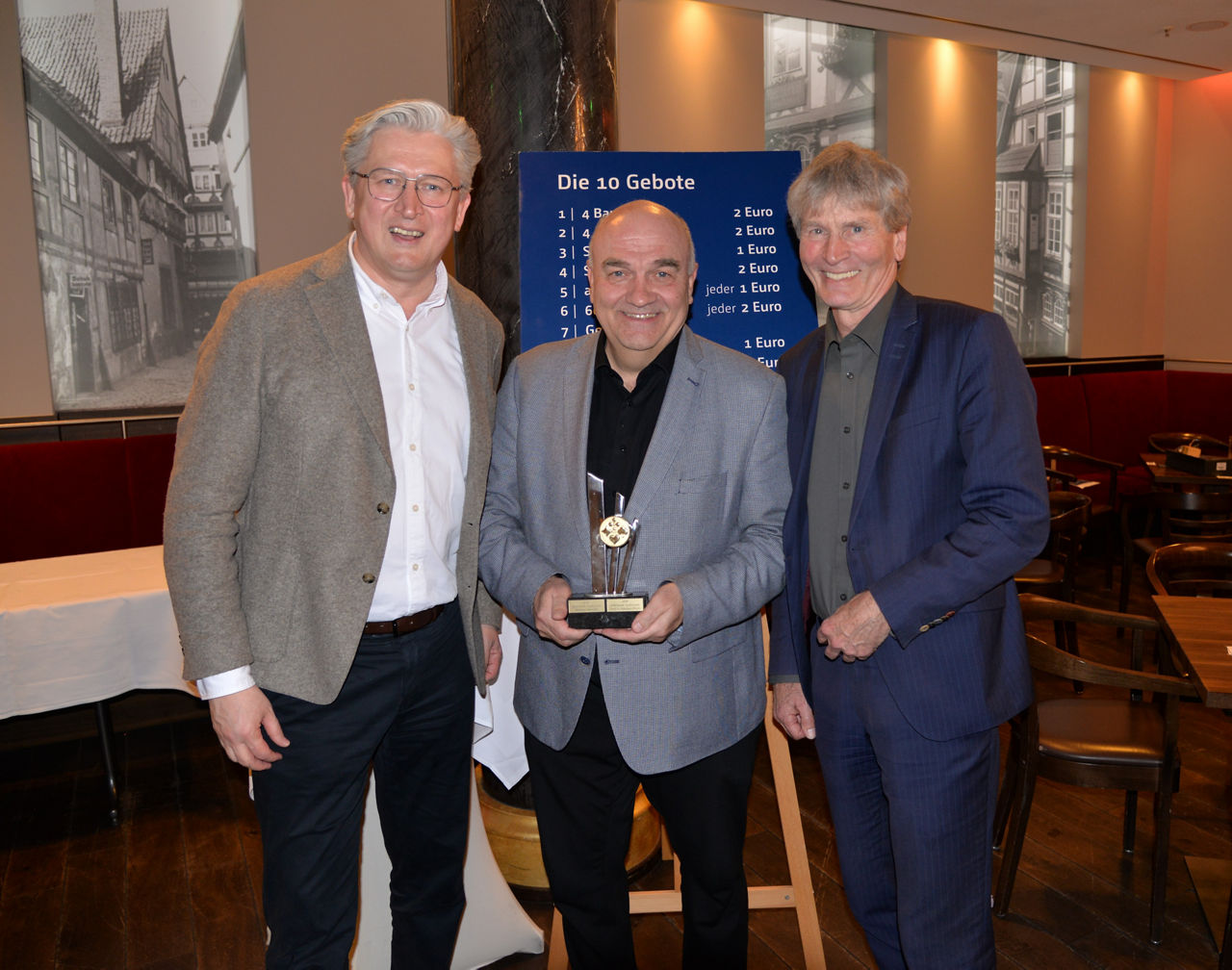 Der Vorstandvorsitzende der VerbundVolksbank OWL und der Skat-Oberschiedsrichter überreichen den Pokal an den Sieger des Volksbank-Skatturniers.