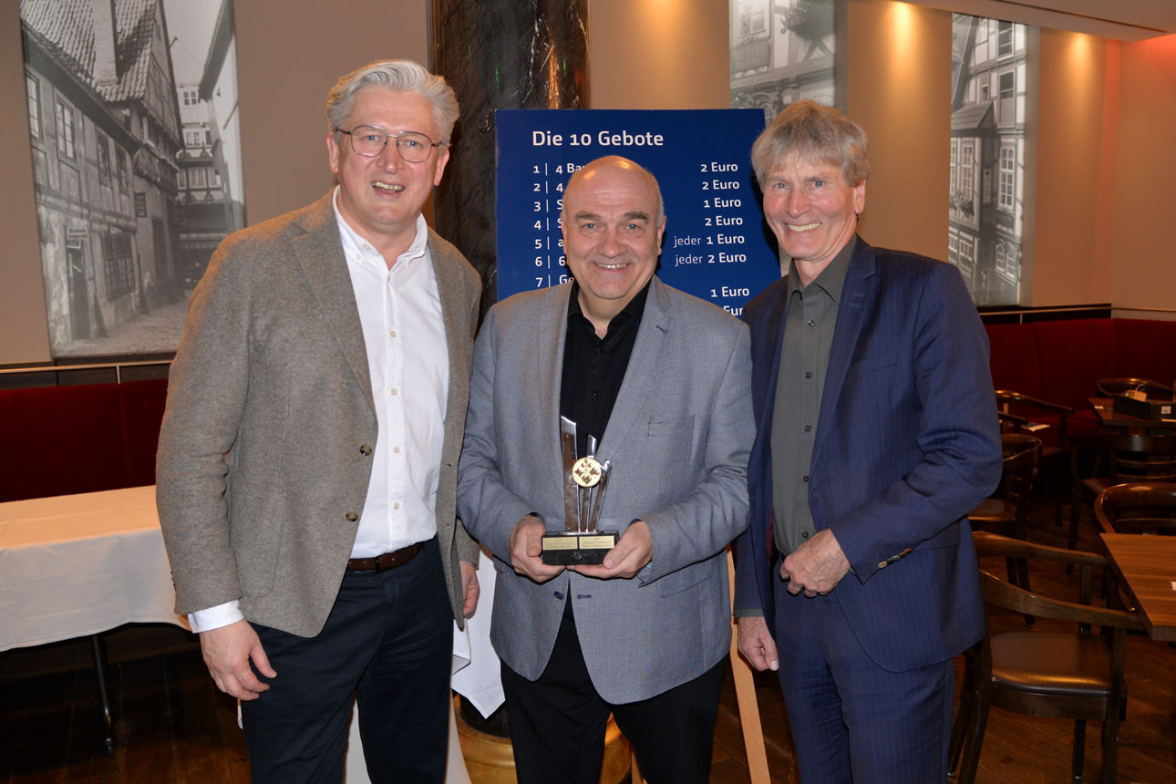 Der Vorstandvorsitzende der VerbundVolksbank OWL und der Skat-Oberschiedsrichter überreichen den Pokal an den Sieger des Volksbank-Skatturniers.