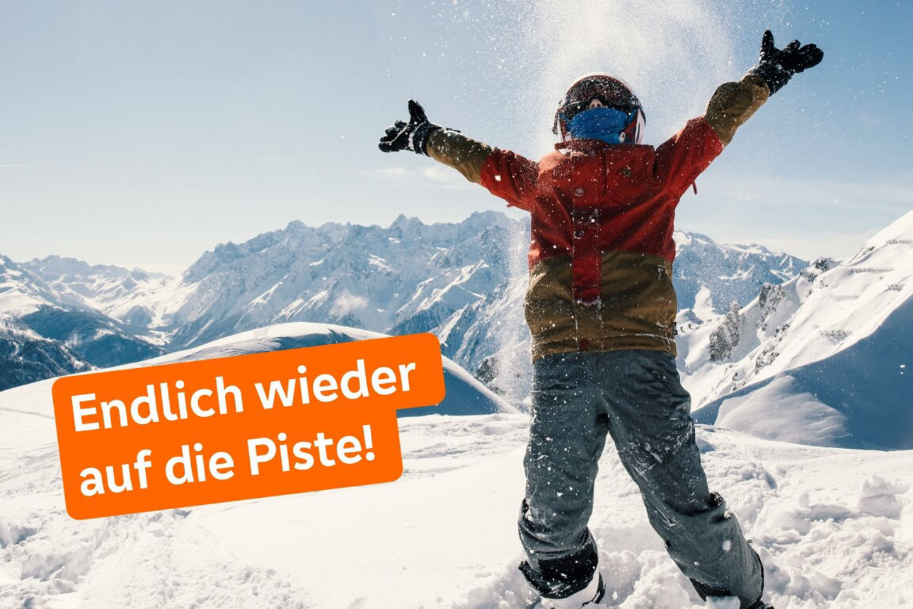 Person im Schnee in Skikleidung wirft Schnee in die Luft mit Bergen im Hintergrund