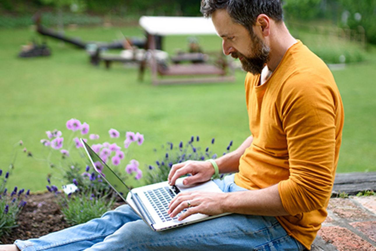 Mann sitzt im Garten am Laptop