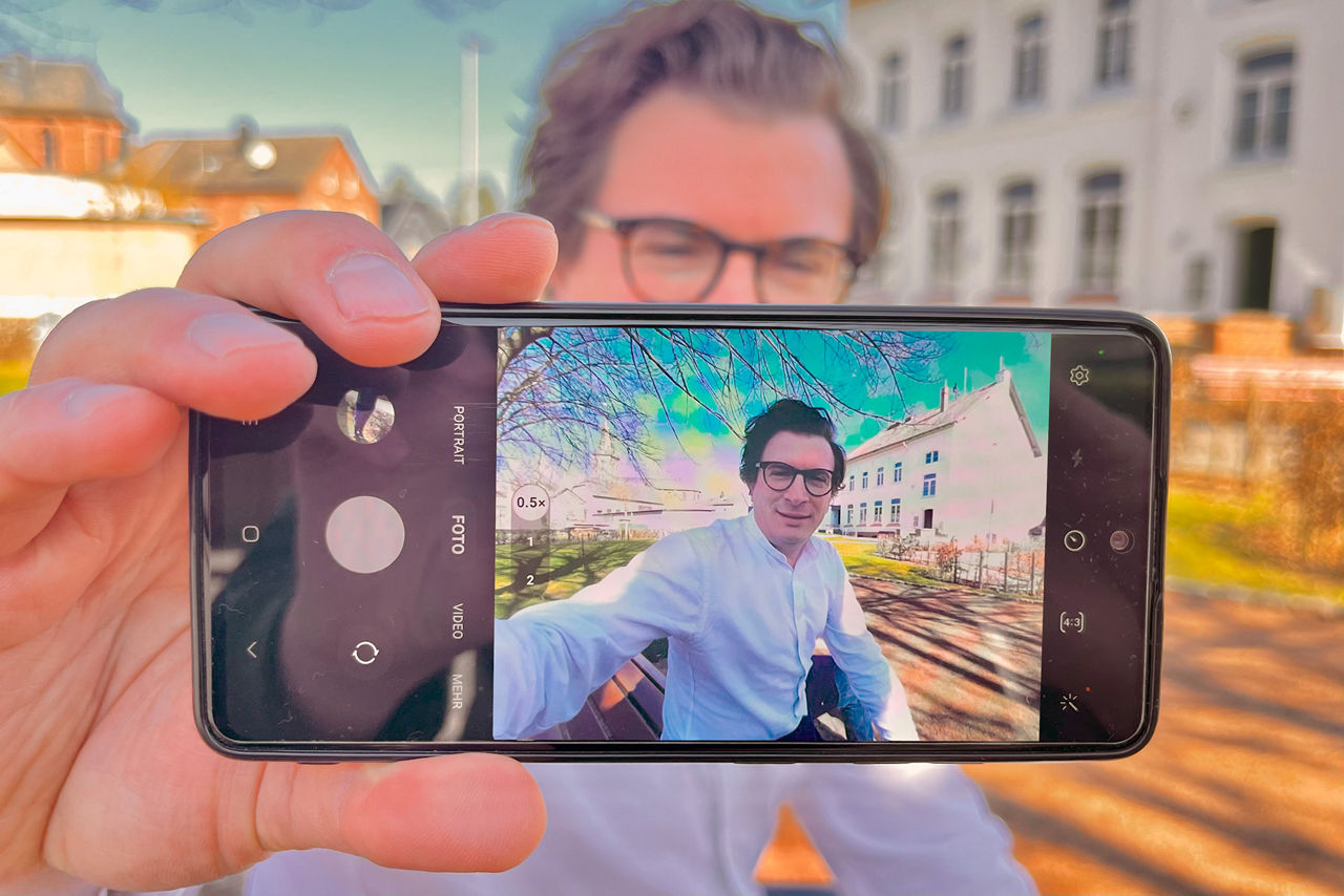 Ein Mann hält ein Handy vor seinem Gesicht hoch und durch die Kamera kann man den Mann sehen