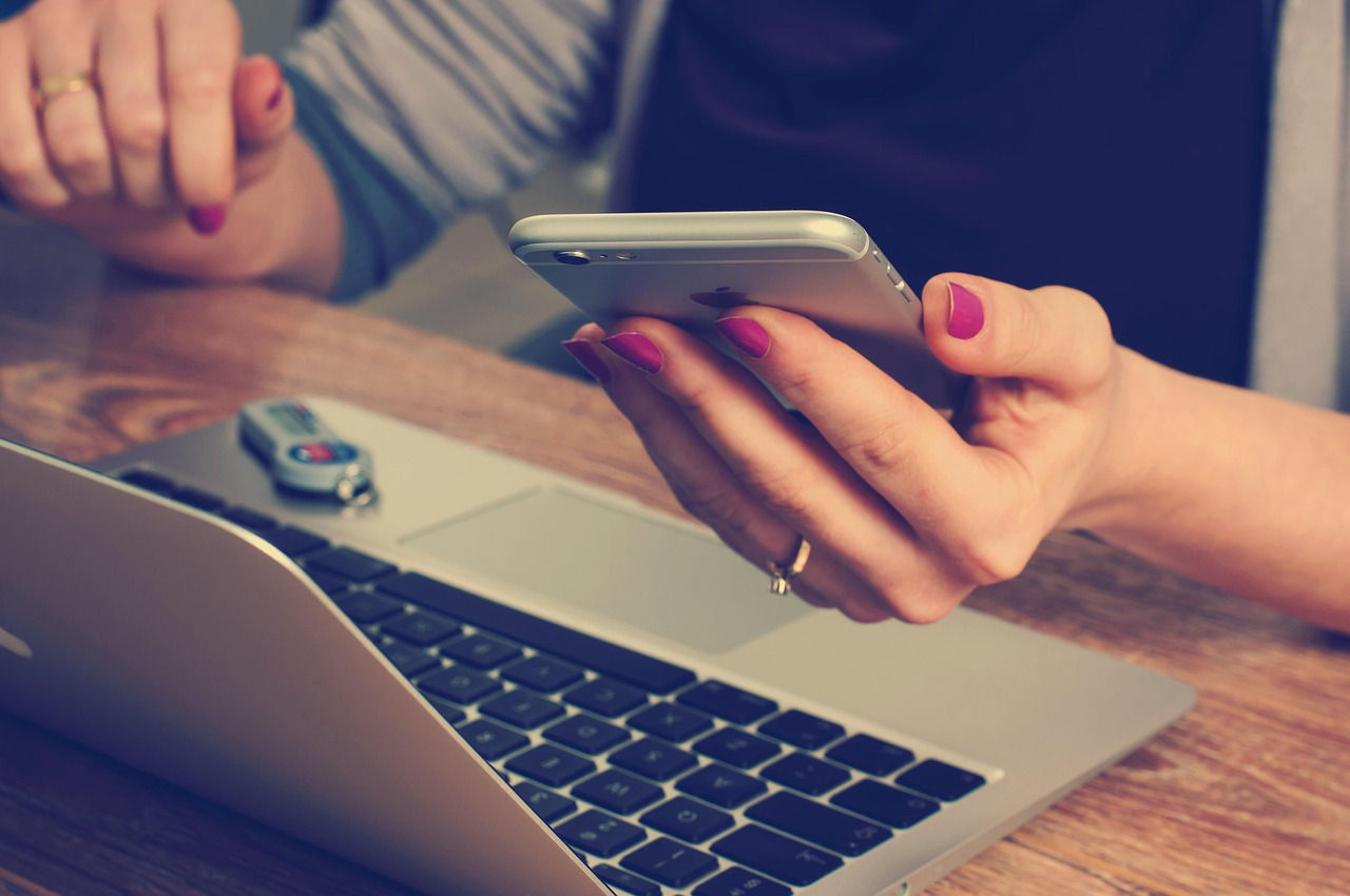 Hand einer Frau mit dem Smartphone darin vor einem Laptop
