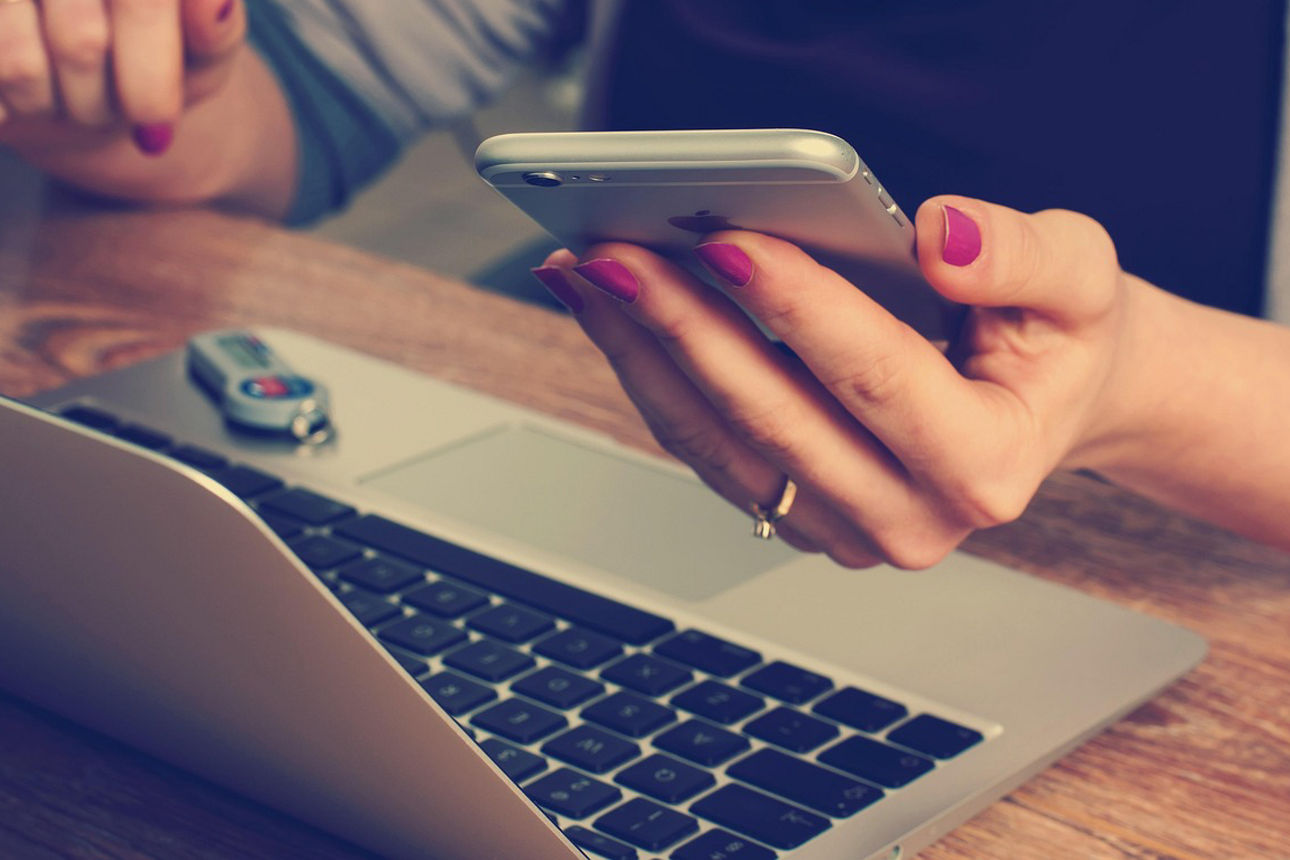 Frau vor Laptop mit Smartphone in der Hand
