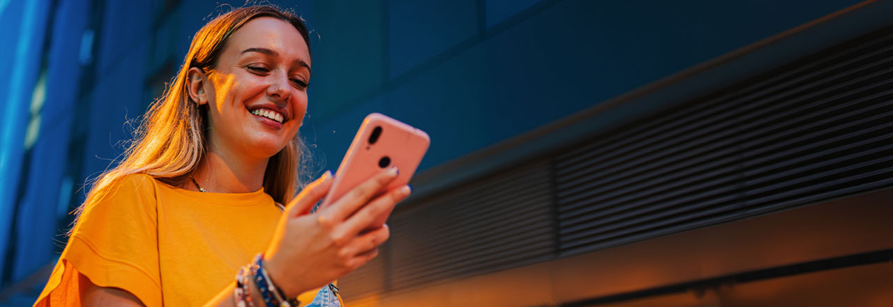 Frau in guckt auf ihr Handy und lächelt.