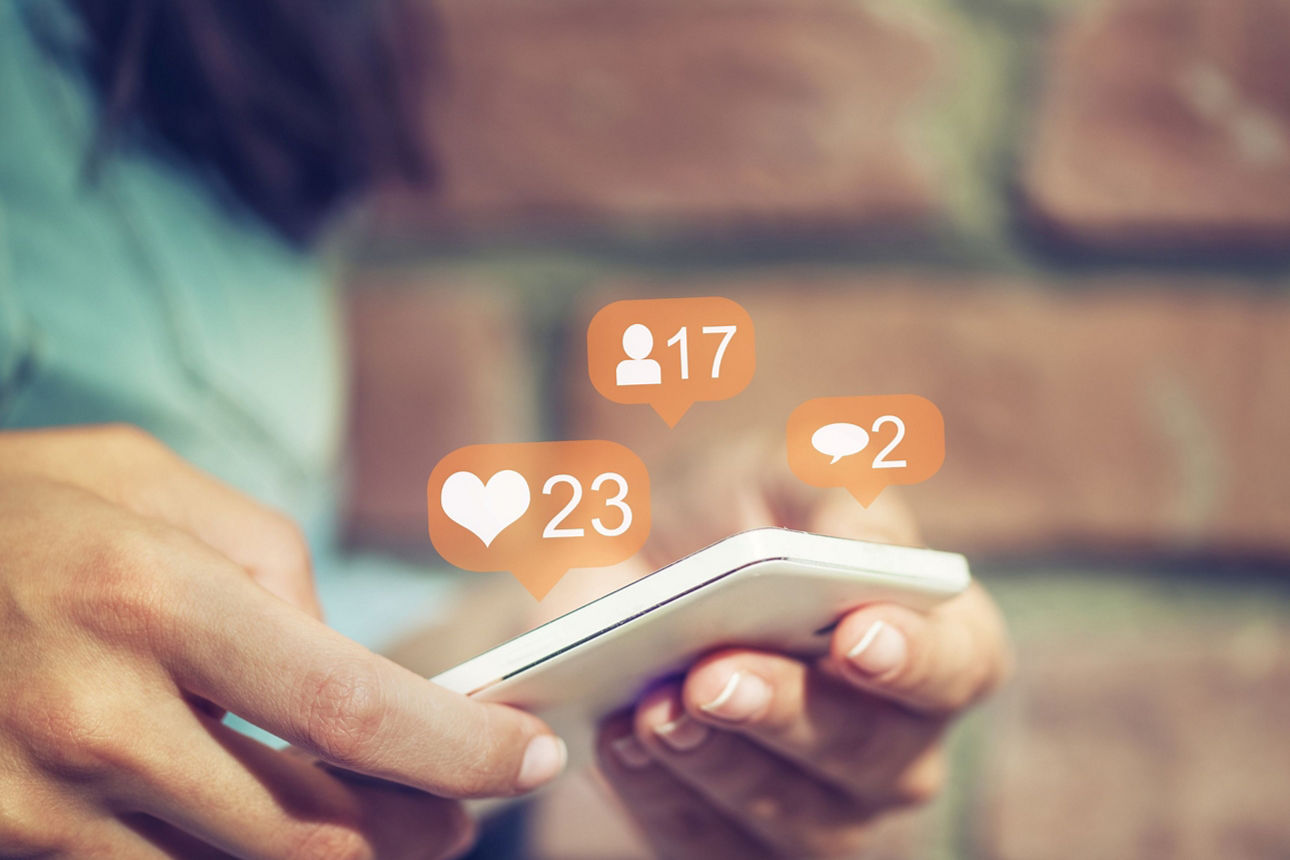 Hände halten ein Smartphone mit der Darstellung digitaler Likes und Follower