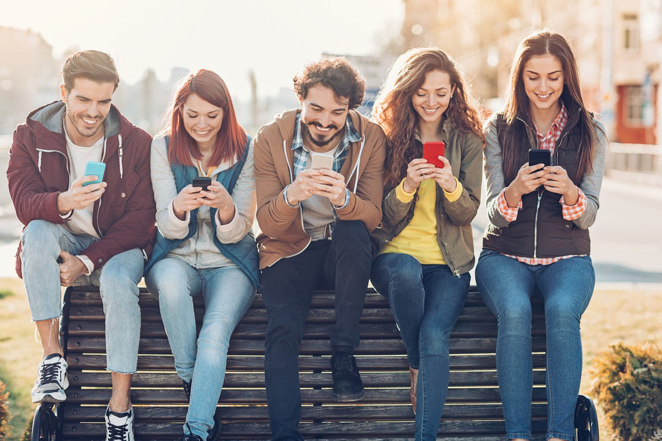 Eine Gruppe Jugendlicher sitzt mit ihren Smartphones auf einer Parkbank.