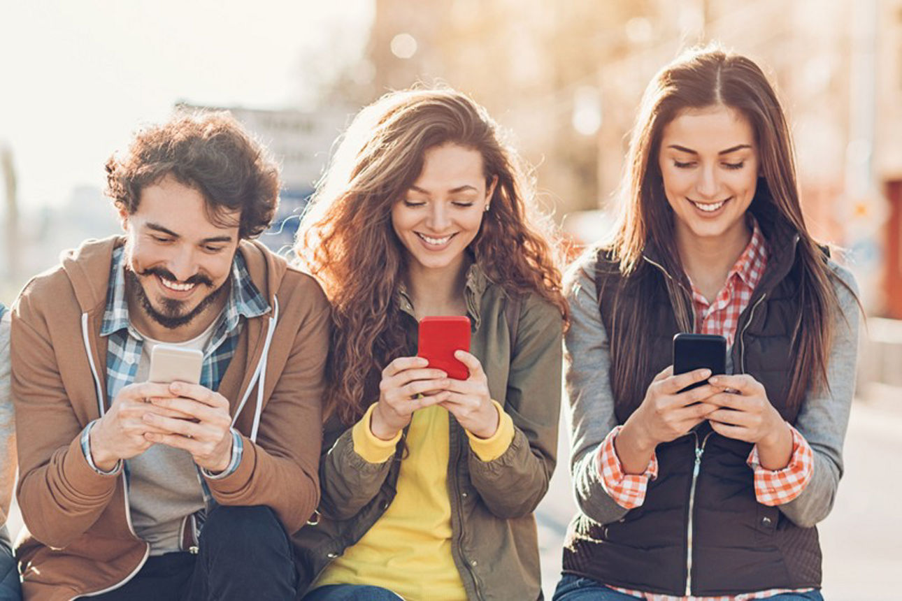 Eine Gruppe Jugendlicher sitzt mit ihren Smartphones auf einer Parkbank.