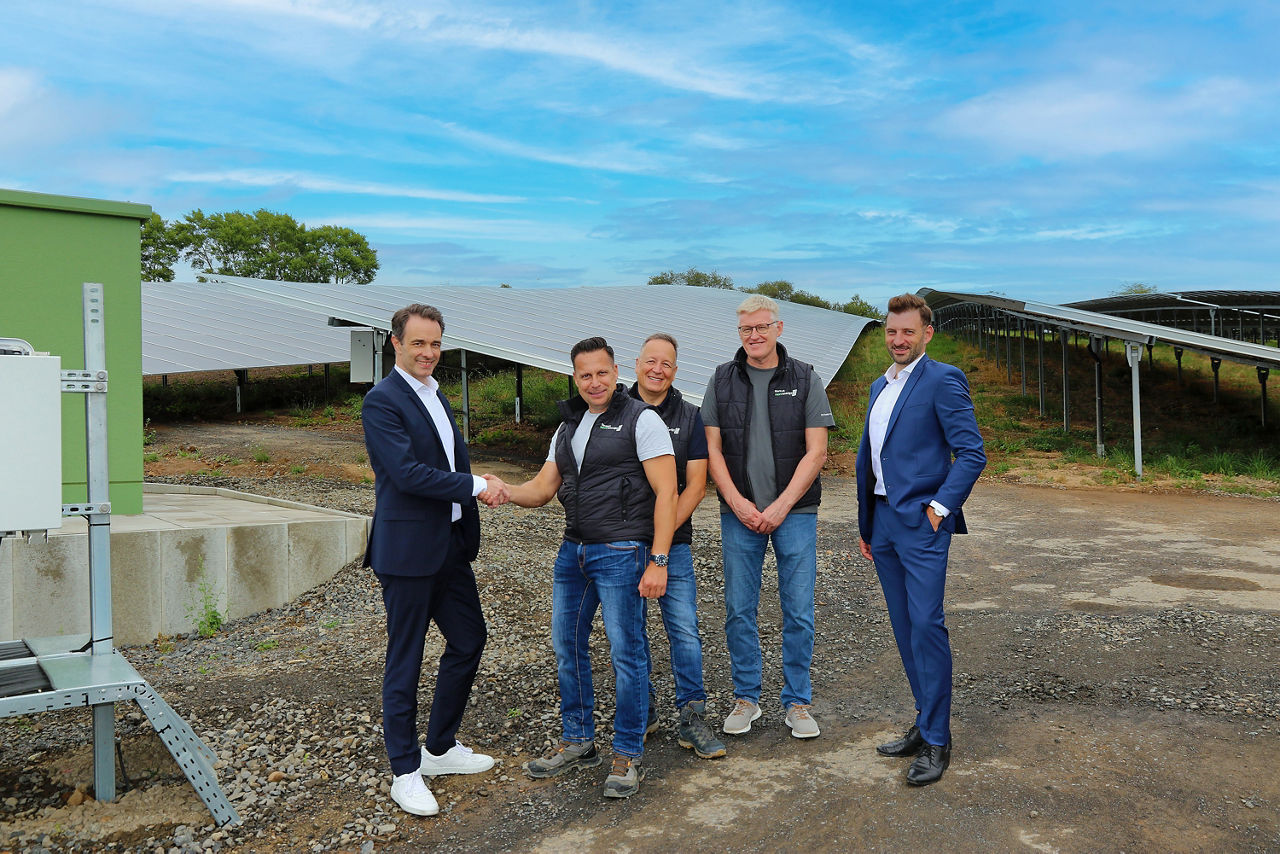 Bankvorstand Lars Schurich und „next energy“-Geschäftsführer Torsten Eurich stehen händeschüttelnd vor dem neu in Betrieb gegangen Solarpark in Großenhausen. Daneben stehen der leitende Projektentwickler Thomas Ott, Finanzen und Controlling Markus Jetzinger und Teamleiter Firmenkunden Marc Bläsing.