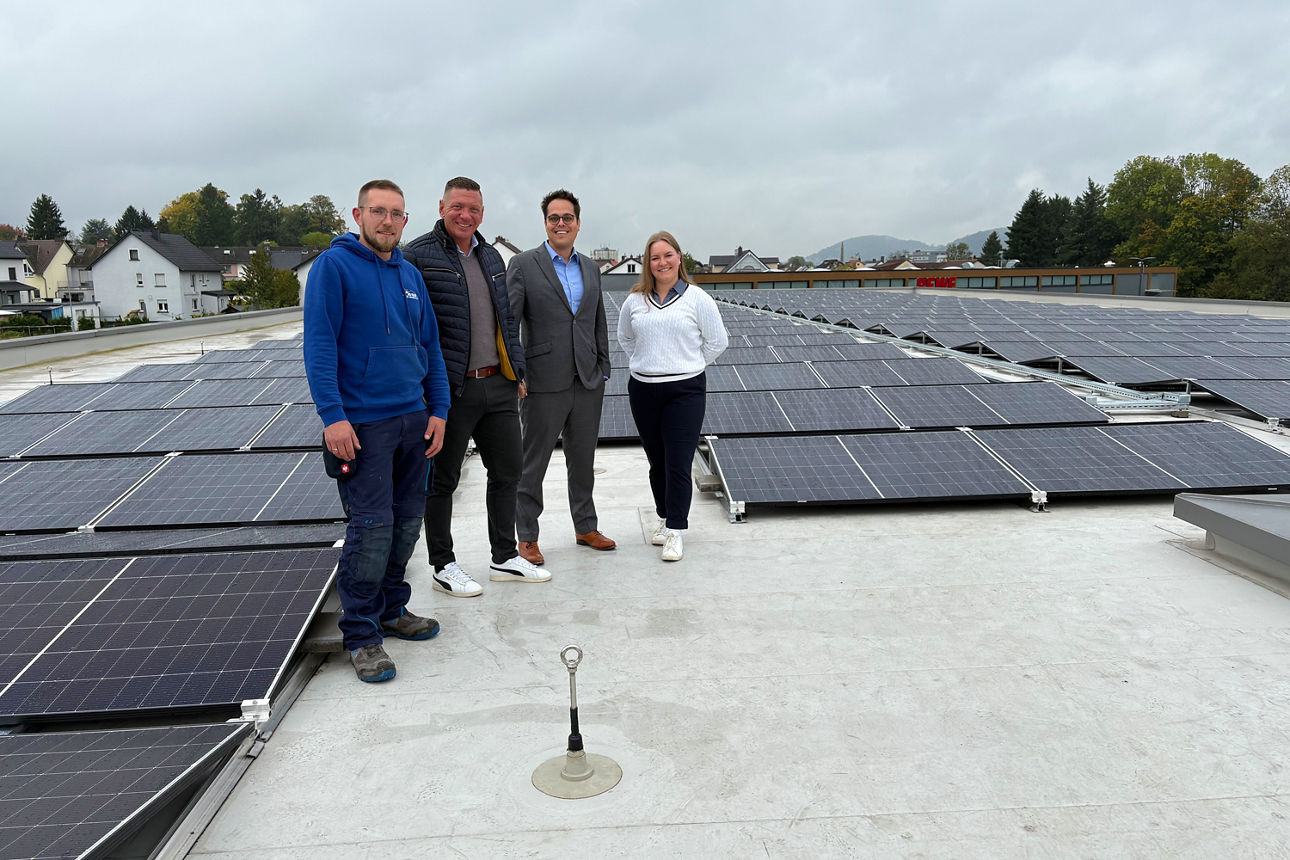 Das Bild zeigt vier Personen auf einem Supermarktdach vor einer Photovoltaik-Anlagen. 