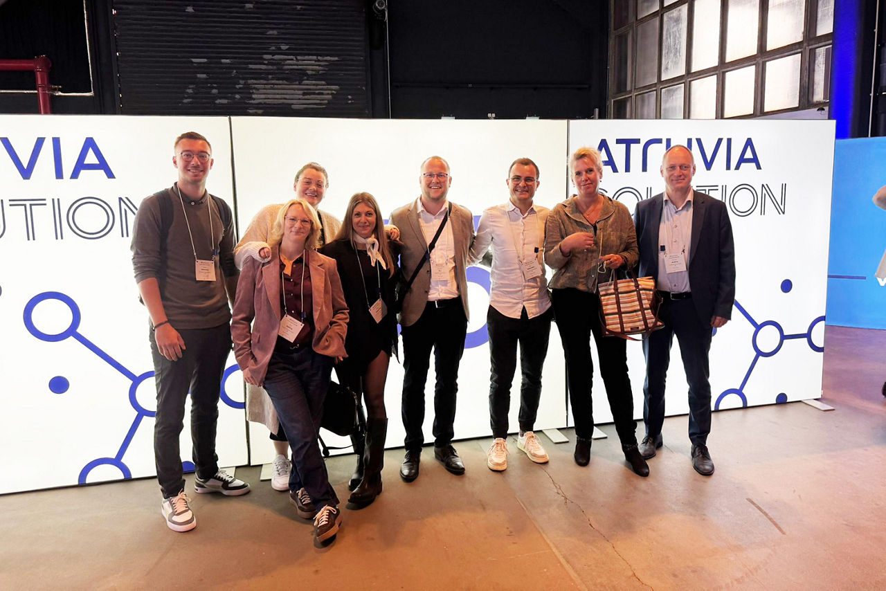 Ein Gruppe aus vier Frauen und vier Männern der Volksbank Schermbeck vor einem Banner der Atruvia zu den Solution Days.