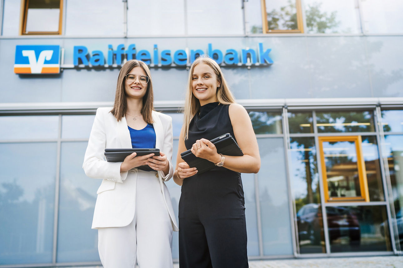 Zwei Frauen mit ihren Tablets vor einer Raiffeisenbank.