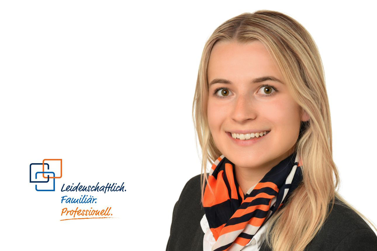 Sophie Stetter, eine junge Frau mit langen blonden Haaren, lächelt freundlich und trägt eine dunkle Jacke mit einem bunten Schal, der orange, blaue und weiße Streifen aufweist.