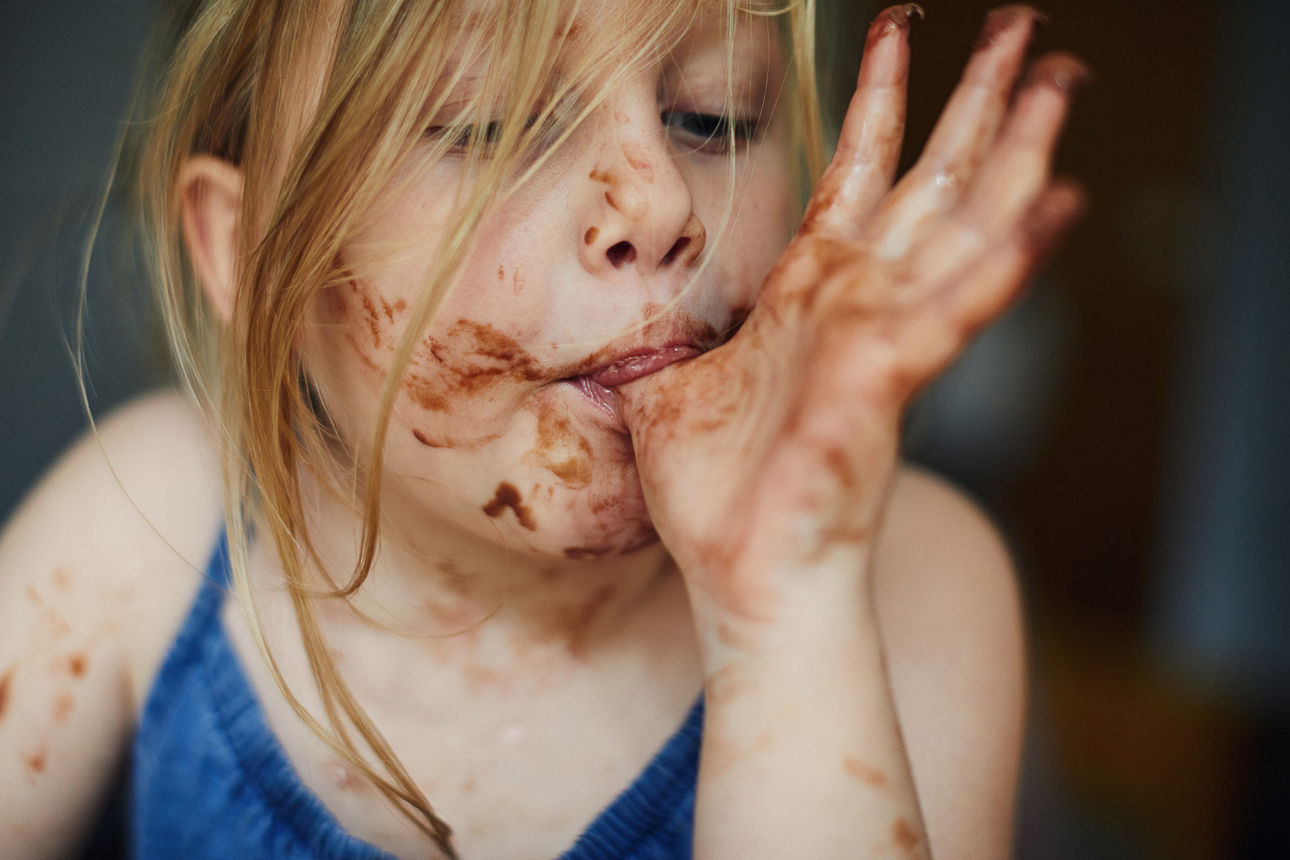 Kind schleckt Schokolade vom Daumen 