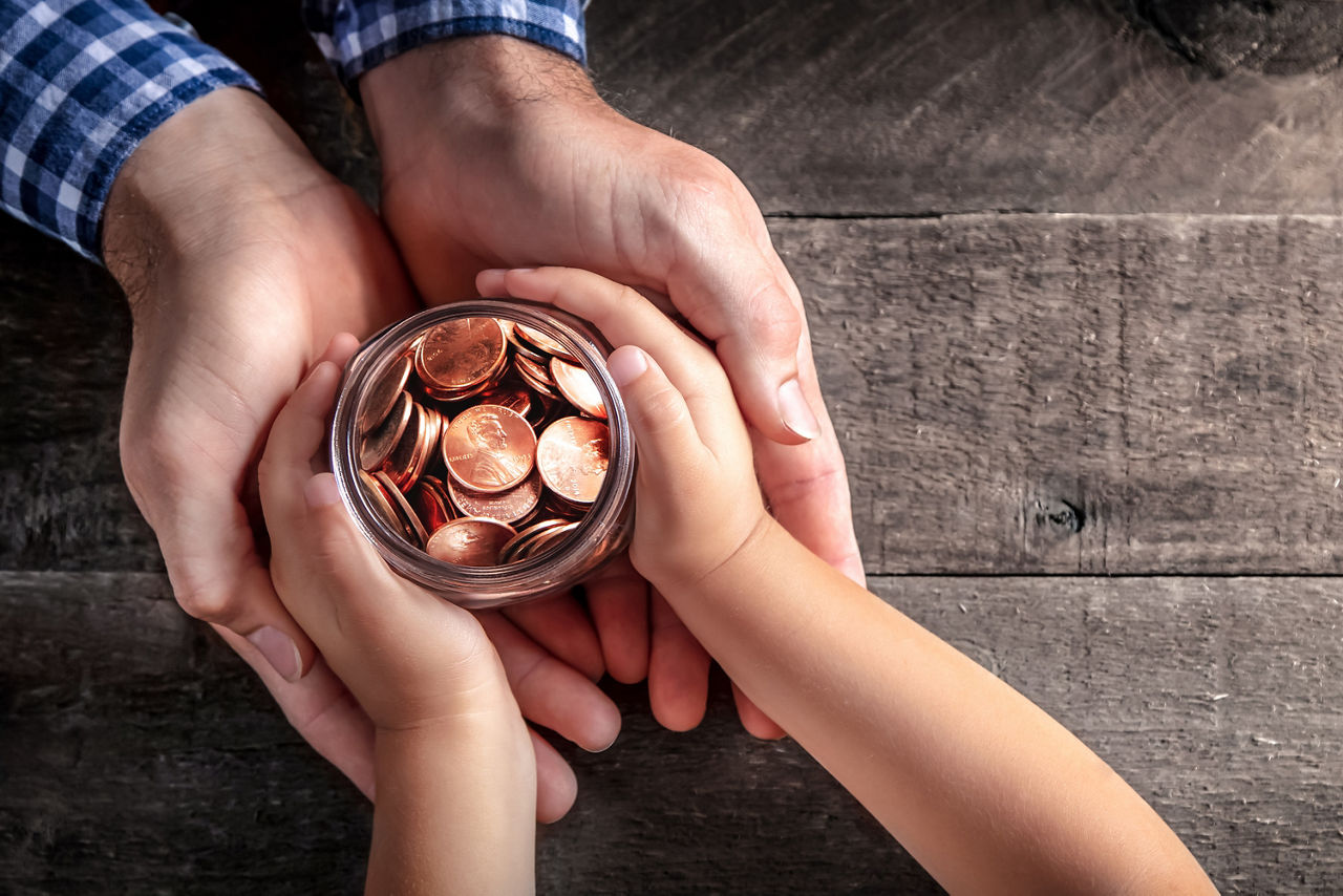 Erwachsenen- und Kinderhände umfassen ein Glas mit Cent-Münzen