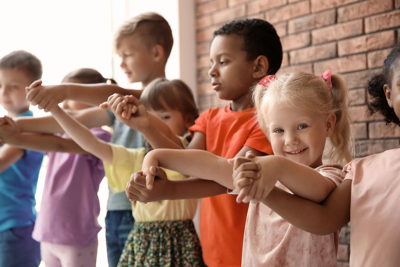 Lächelndes blondes Mädchen steht in Reihe mit anderen Kindern, alle halten sich an den Händen