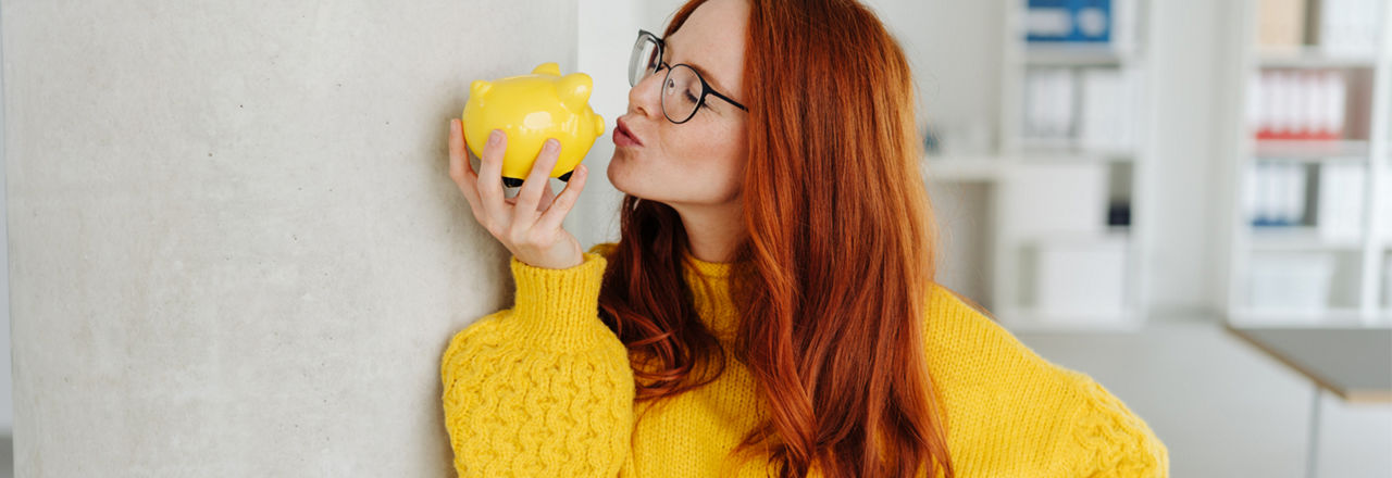 Frau mit gelbem Pulli küsst ein gelbes Sparschwein.