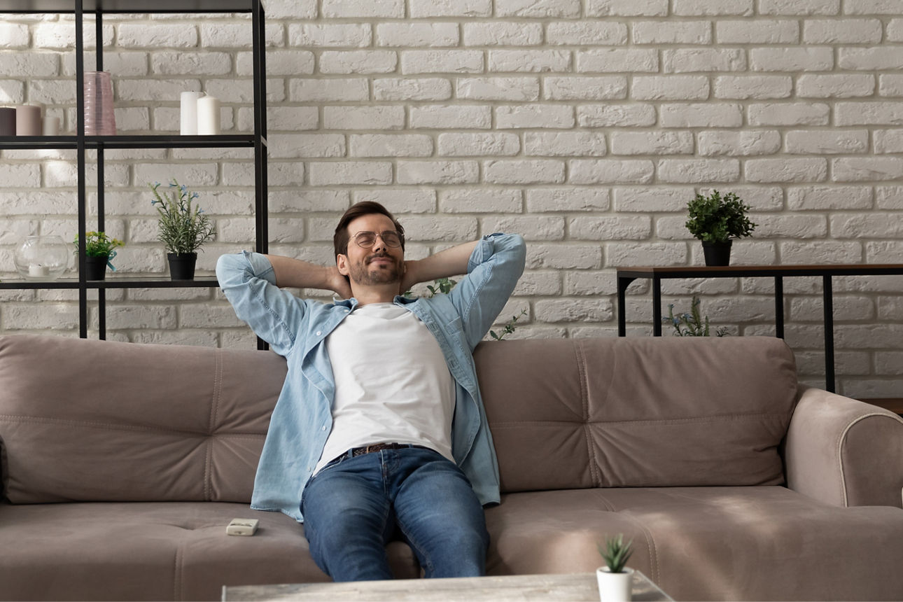 Ein Mann sitzt mit geschlossenene Augen entspannt auf dem Sofa.