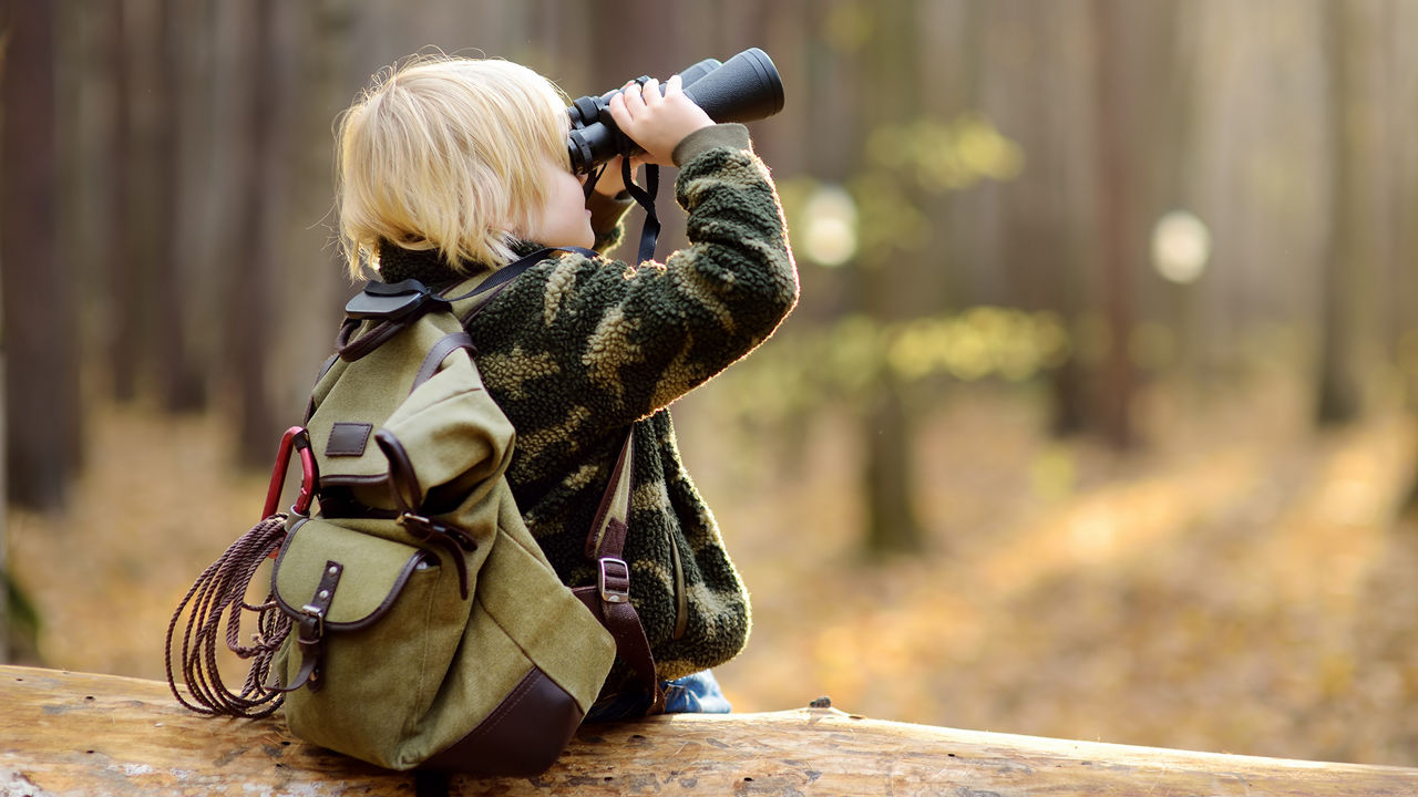 Junge sitzt auf Baumstamm und benutzt Fernglas