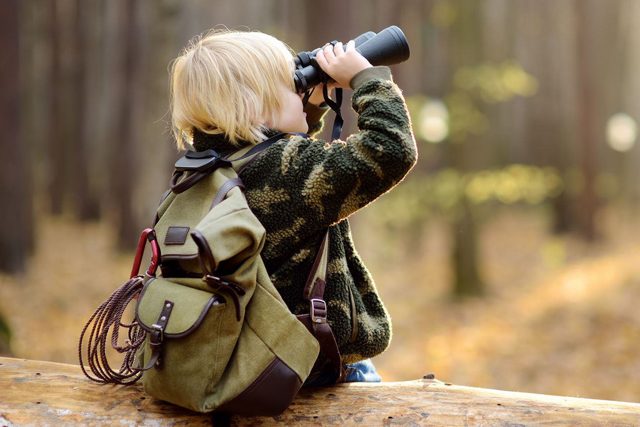 Junge sitzt auf Baumstamm und benutzt Fernglas