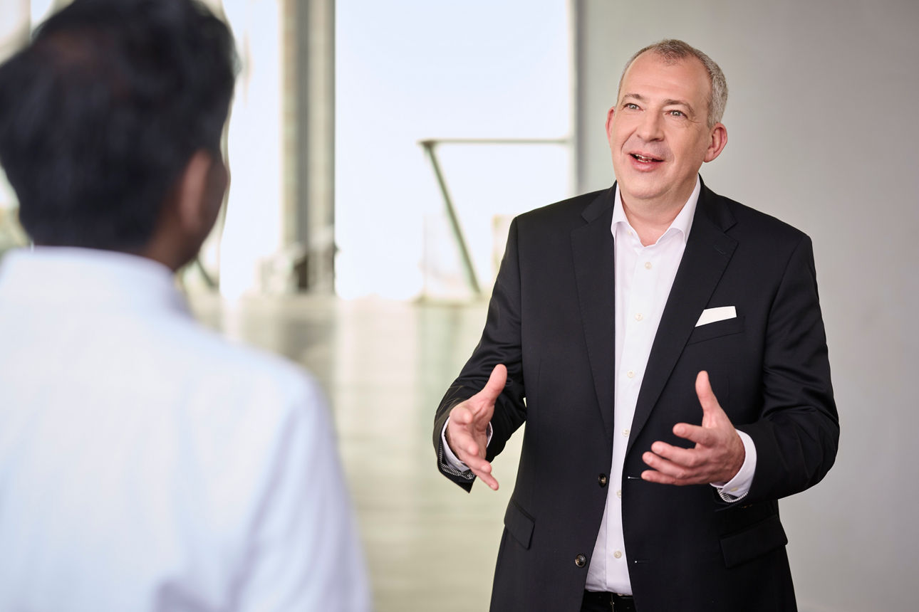 Mann im Anzug im Gespräch mit einer weiteren Person