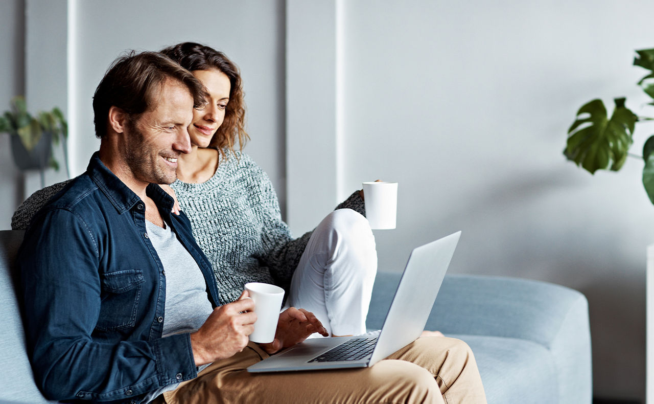 Mann und Frau sitzen mit Tasse und einem Laptop auf einem Sofa