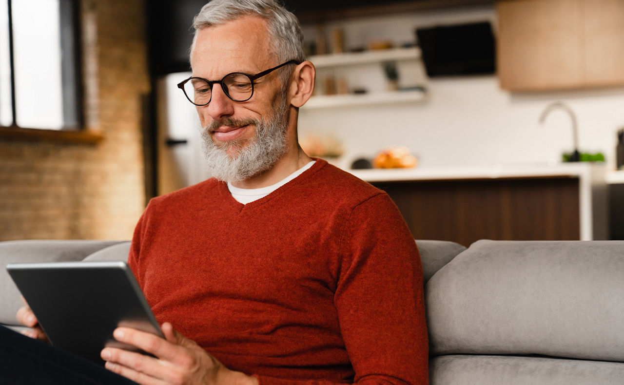 Mann mittleren Alters sitzt mit einem Tablet in der Hand auf einem Sofa