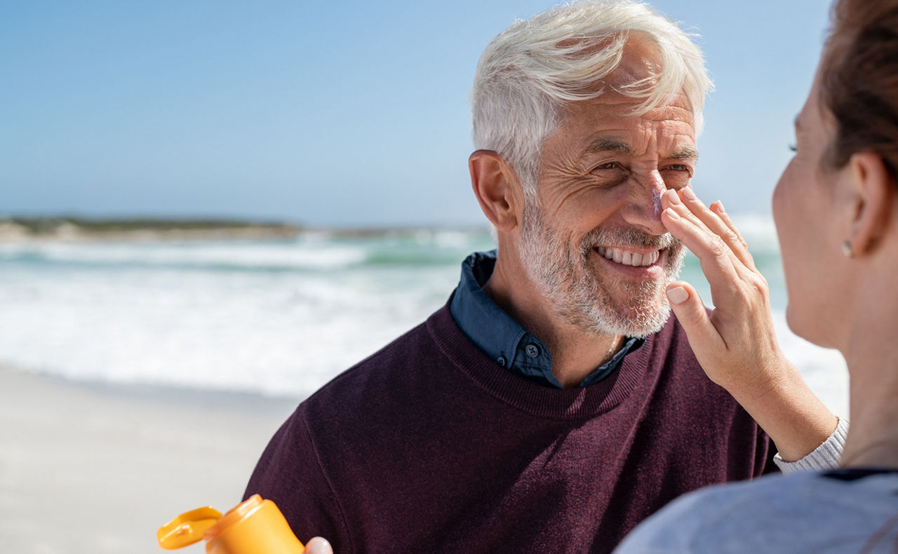 Eine Frau cremt einen Mann die Nase mit Sonnencreme am Strand ein