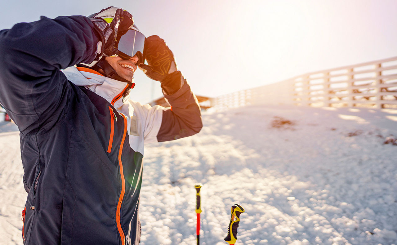 Skifahrer steht am Pistenrand und setzt sich eine Skibrille auf
