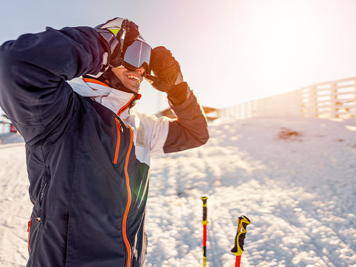 Skifahrer steht am Pistenrand und setzt sich eine Skibrille auf