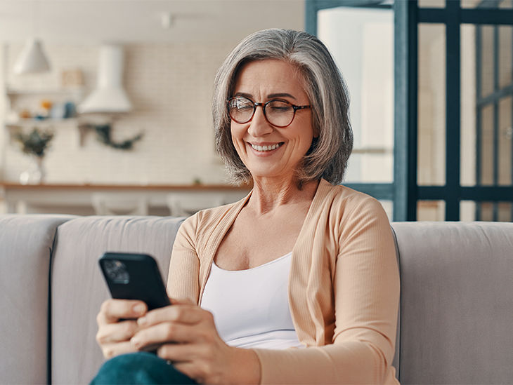 Frau sitzt auf dem Sofa und hält ein Handy in der Hand