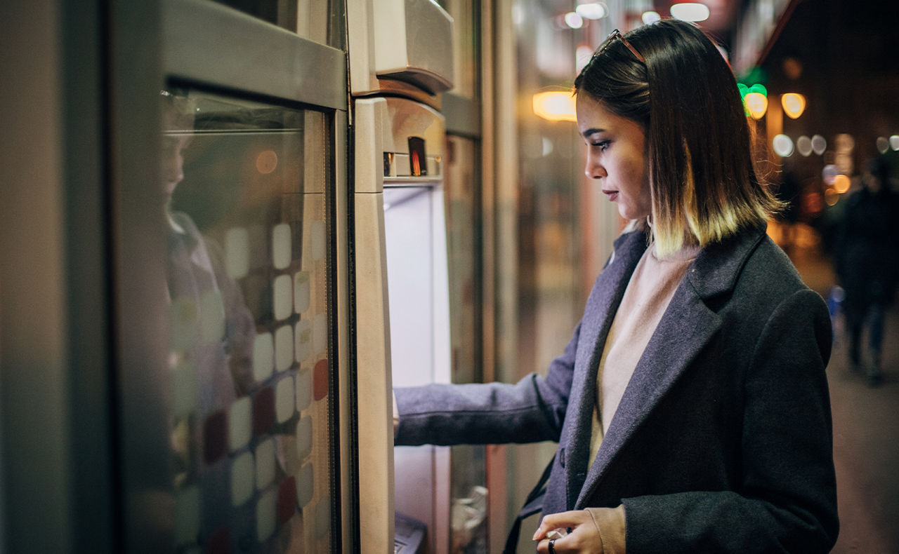 Frau hebt abends Geld am Automaten ab