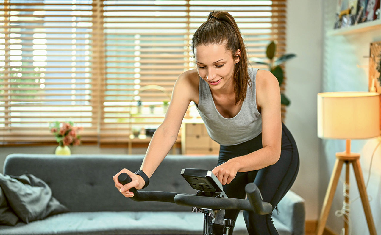 Junge Frau auf einem Ergometer in ihrem Wohnzimmer