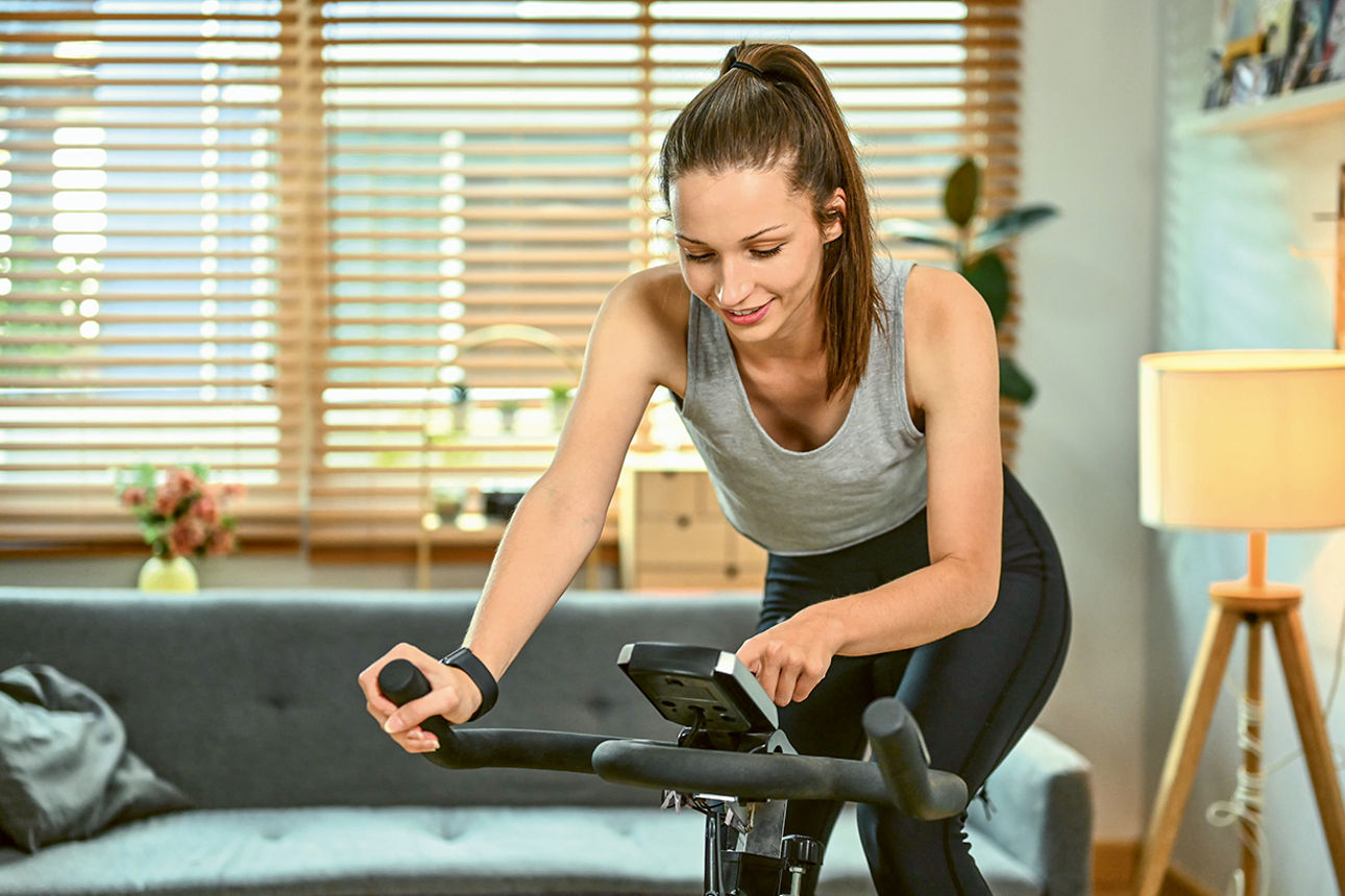 Junge Frau auf einem Ergometer in ihrem Wohnzimmer