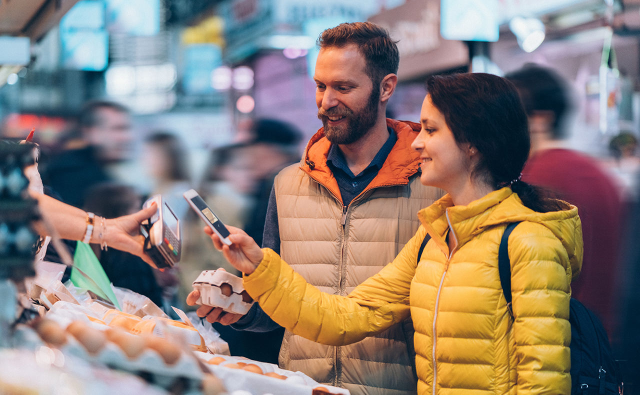 Mann und Frau bezahlen ihren Wochenmarkteinkauf mit dem Smartphone