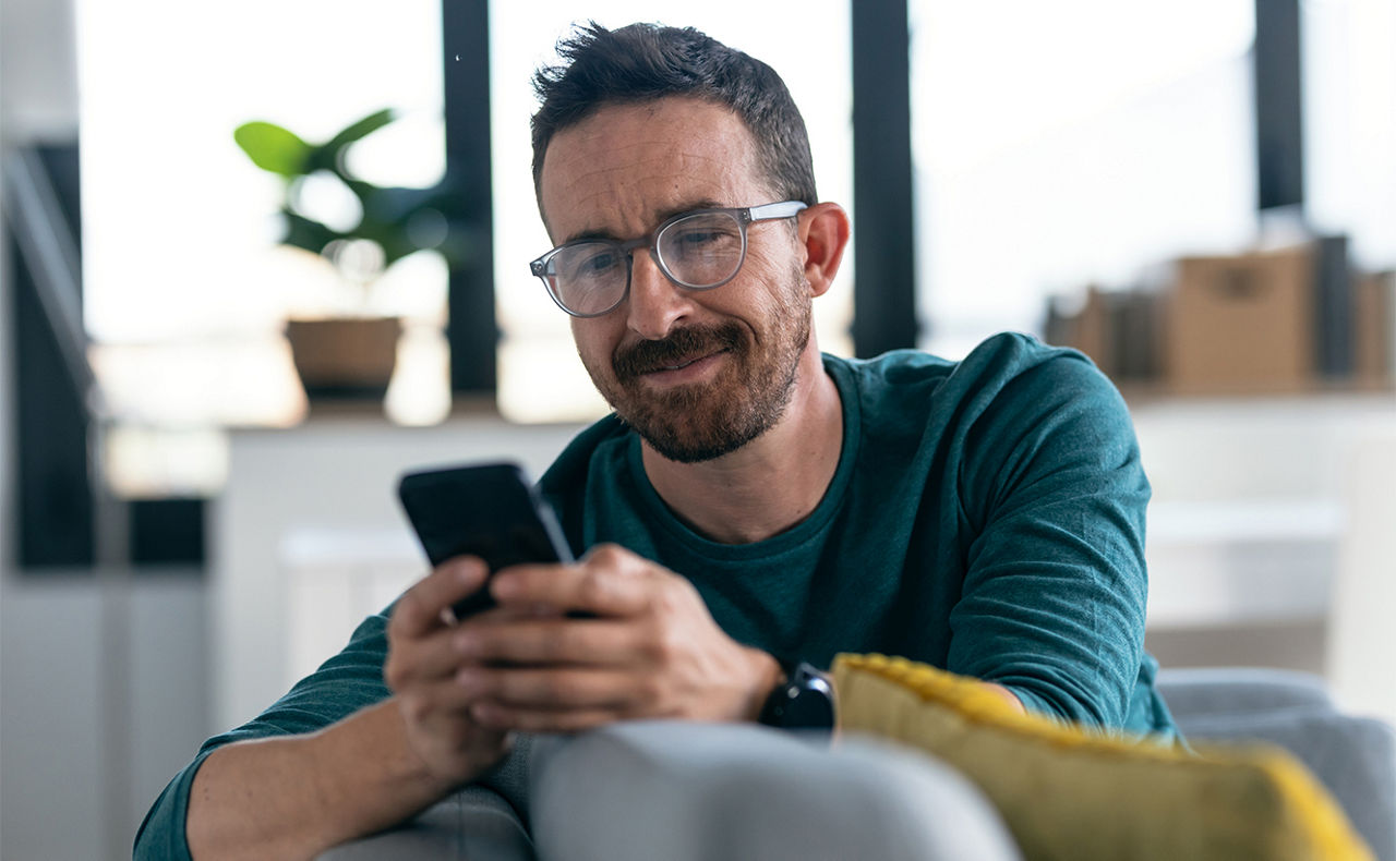 Mann sitzt auf einem Sofa mit einem Handy in der Hand
